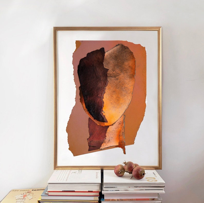 A dramatic, brown-orange golden framed art print of an abstract head in all shades of dark wood and blazing orange. A reddish spot spills out the torn paper, random-shaped Halloween pumpkin background. The wall art is arranged on a pile of books.