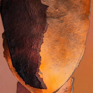 A dramatic detail of a vivid brown-orange  abstract head in all shades of dark wood and blazing orange. A reddish drop spills out from the torn paper faded persimmon background. Sharp, coarse contours in flame orange separate the ripped paper layers.