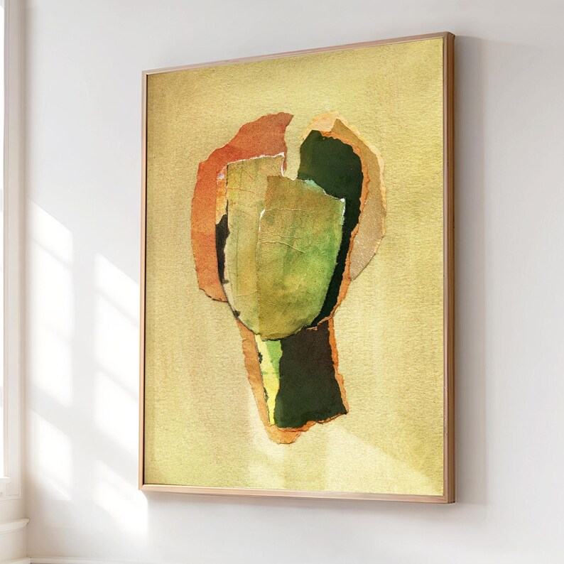 May include: Abstract art print in a wooden frame. The artwork features layered paper in shades of green, orange, and yellow against a light yellow background. The frame is a light brown color. The artwork is displayed on a white wall.
