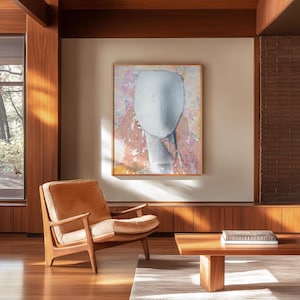 May include: A rectangular framed wall art piece featuring a central pale blue oval shape against a textured background of mottled pink, orange, and white tones. The artwork is displayed in a thin wooden frame and hangs on a plain wall.