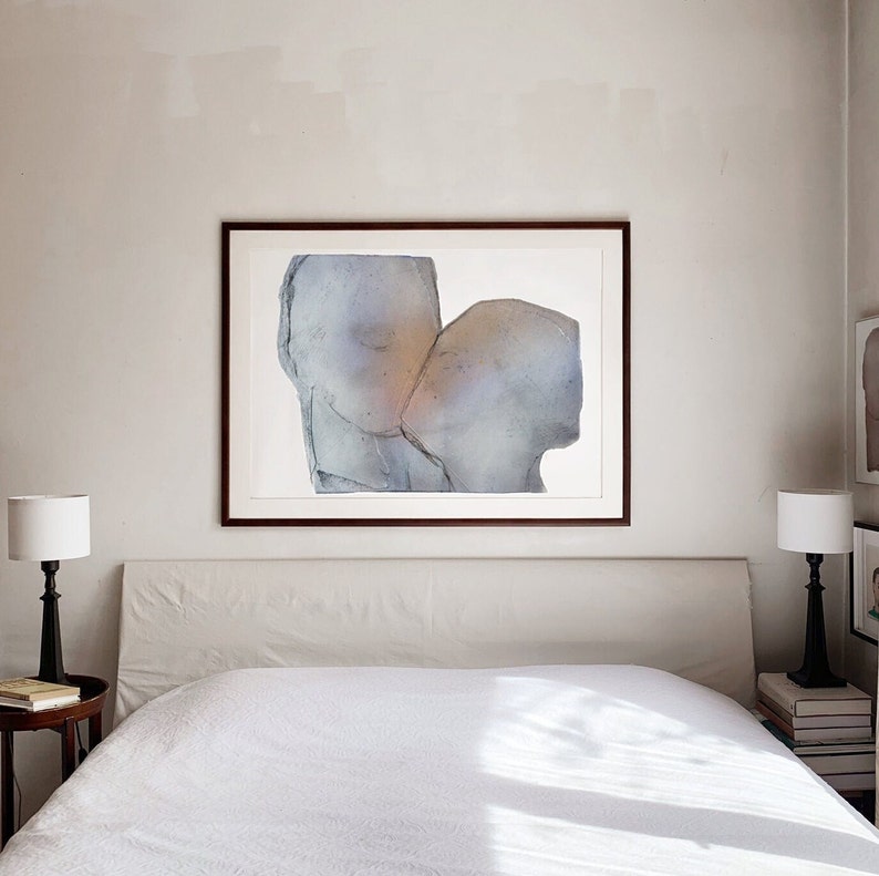 A bedroom wall decor with a dark wood framed high quality art print of a romantic abstract portrait of a love couple kiss in greige, dovetail and silver grey on white. The torn paper have grungy edges and a mural feel. The kiss glows opaque gold.