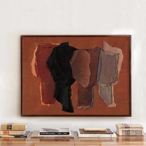 Puede incluir: Obra de arte abstracta en un marco de madera. La obra presenta papel rasgado en capas en tonos de rojo, negro y morado sobre un fondo marrón rojizo. El marco es de color marrón oscuro. Se ven libros sobre una superficie de madera debajo.