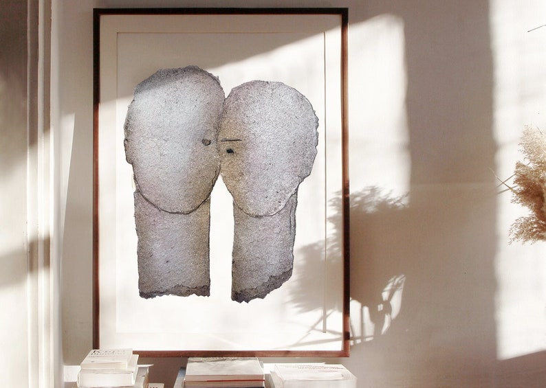 A dark wood framed high quality art print of a romantic abstract portrait of a love couple in shades of grey with silver finish on white. The two heads are composed of torn rough paper layers with exposed grungy edges and two eyes for accent.