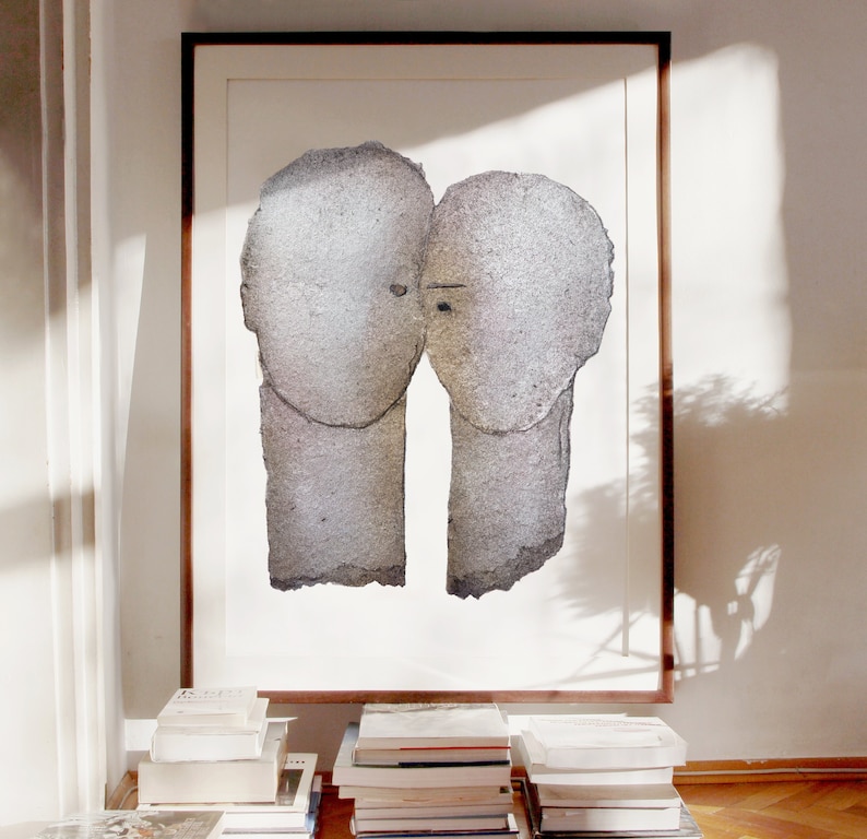 A decor with dark wood framed high quality art print of a romantic abstract portrait. It is a love couple in shades of grey with silver finish on white. The heads are composed of torn rough paper layers, exposed grungy edges and two eyes for accent.