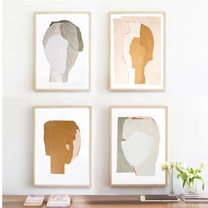 A wall decor with a set of four light wood framed high quality art prints of abstract portraits in of-white, pale pink, greige and honey. One has a red minimal eye and one has a pencil drawn one. The set is balanced and neutral, best for wall decor.