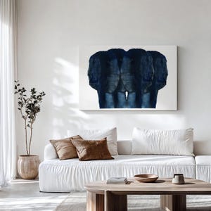 Puede incluir: Un sof&aacute; blanco con cojines marrones se encuentra frente a una pared blanca con una pintura abstracta azul colgada encima. Una planta en maceta est&aacute; en el lado izquierdo de la imagen.