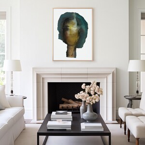May include: A watercolor painting of a person's face with a blue and green background. The painting is framed and hanging on a white wall above a fireplace.