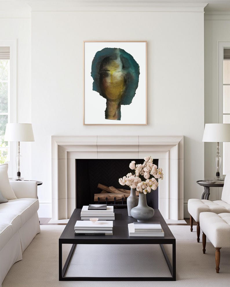 May include: A watercolor painting of a person's face with a blue and green background. The painting is framed and hanging on a white wall above a fireplace.