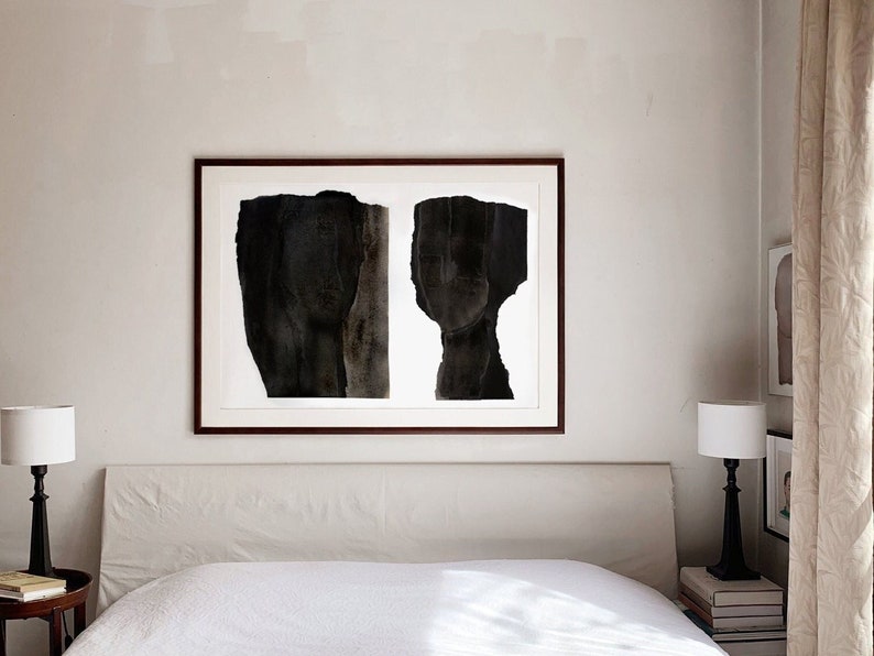 A bedroom wall decor with a maple wood framed, high quality art print of a modern abstract double portrait in asphalt black and dark brown on white, composed of a torn paper layers with grungy edges and a water color effect.