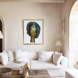 A tie-a room-together high quality light framed art print of a big sized abstract room-tying female portrait in shades of petrol blue, golden, yellow and black. The torn-to-shape laid paper piece has rough edges. The grainy texture is spray painted.