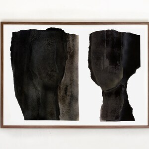 A dark wood framed, high quality art print of a modern abstract double portrait in asphalt black and dark brown on white, composed of a torn paper layers with grungy edges. The texture has a water color effect. Shades of tan browns remind of a nose.