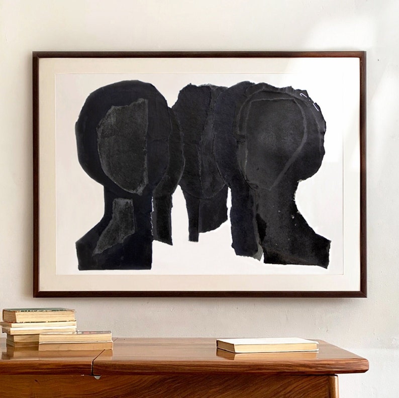 A wall decor with a large statement art in shades of brushed eerie black and dovetail grey. This black framed group portrait has five abstract heads. The overlapping layers of torn paper, finished in opaque shades of black are arranged in an arch.