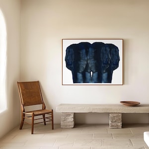 Puede incluir: Una pintura abstracta azul de tres figuras en un marco blanco colgada en una pared beige sobre un banco de hormig&oacute;n. Una silla de madera est&aacute; en primer plano.