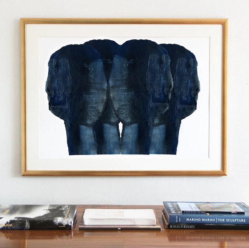 Puede incluir: Una impresi&oacute;n de arte abstracto enmarcada con tres caras de acuarela azul y blanca. La impresi&oacute;n est&aacute; colgada en una pared blanca sobre una mesa de madera con libros.