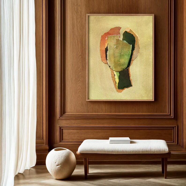 May include: Abstract art print in a wooden frame. The artwork features a collage of green, orange, and black shapes on a light yellow background. The print is displayed on a wood-paneled wall above a bench with a white cushion.