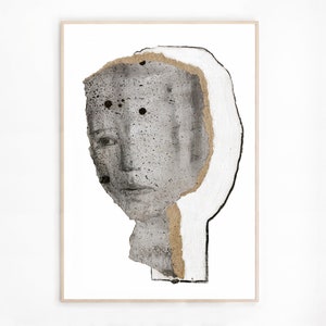 A golden framed high quality statement art print of a modern abstract portrait in shades of gray. A layer of ripped thick paper has golden ochre rough edges and graphite sketched facial features. A bigger head shape behind is outlined with charcoal.