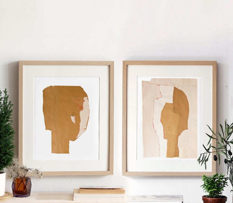 A neutral wall art with two maple wood framed high quality art prints of abstract portraits in pale peach and hues of desert sand yellow. Minimal eyes. The layers of ripped paper have rough edges. The set is balanced and neutral, best for wall decor.