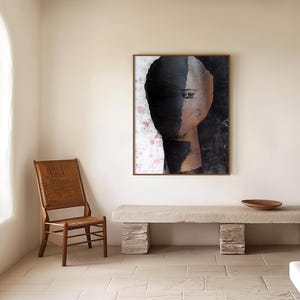 May include: Abstract art print of a face with black and white paint on a white background with pink floral accents. The print is framed in a brown wood frame and is hanging on a white wall.