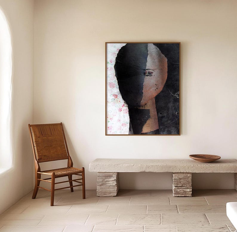 May include: Abstract art print of a face with black and white paint on a white background with pink floral accents. The print is framed in a brown wood frame and is hanging on a white wall.