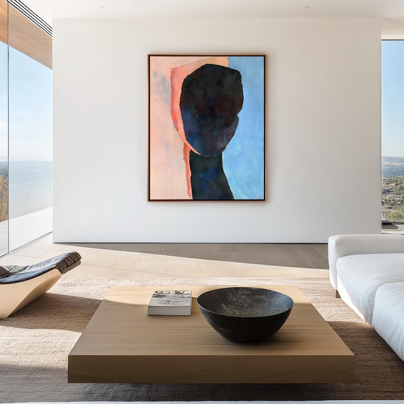 K&ouml;nnte beinhalten: Abstrakte Malerei eines Gesichts in Rosa-, Blau- und Schwarzt&ouml;nen, die an einer wei&szlig;en Wand in einem modernen Wohnzimmer mit einem Holz-Couchtisch und einem wei&szlig;en Sofa h&auml;ngt.
