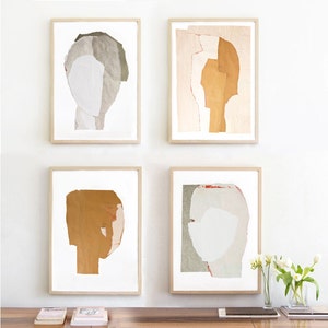 A wall decor with a set of four light wood framed high quality art prints of abstract portraits in of-white, pale pink, greige and honey. One has a red minimal eye and one has a pencil drawn one. The set is balanced and neutral, best for wall decor.