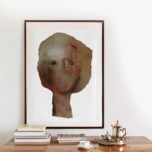 A wall decor with a high quality art print of a modern female portrait in maroon, beige, brown and grey. Two spray painted thick paper layers are torn to shape, with rough edges. A vague nose, scratched off the paint, hair line and two black eyes.