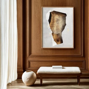 May include: A framed abstract art print with a brown and gold paper design on a white background. The print is hanging on a wood panel wall.