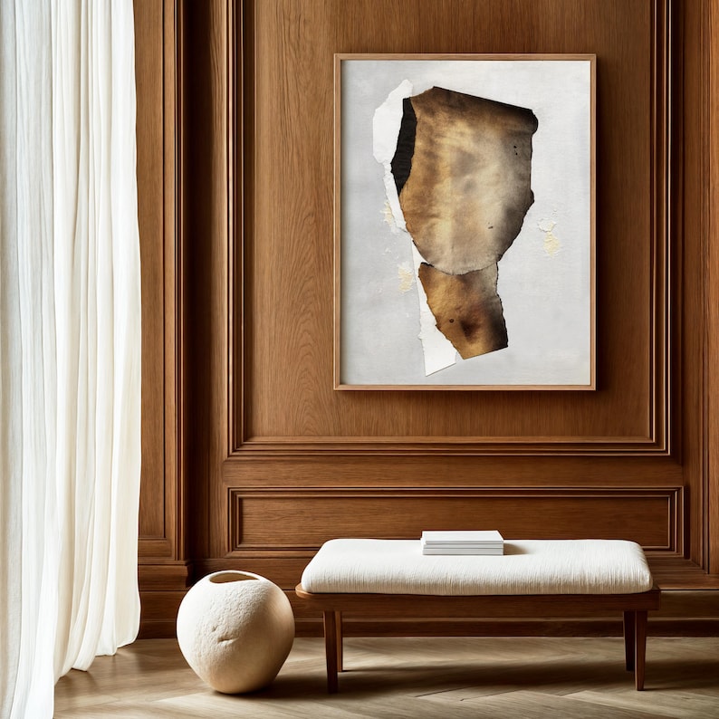 May include: A framed abstract art print with a brown and gold paper design on a white background. The print is hanging on a wood panel wall.