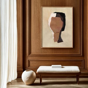 May include: Abstract art print featuring a collage of neutral tones, including beige, brown, and black, within a wooden frame. The artwork is mounted on a wood-paneled wall, complemented by a white bench and a decorative vase.