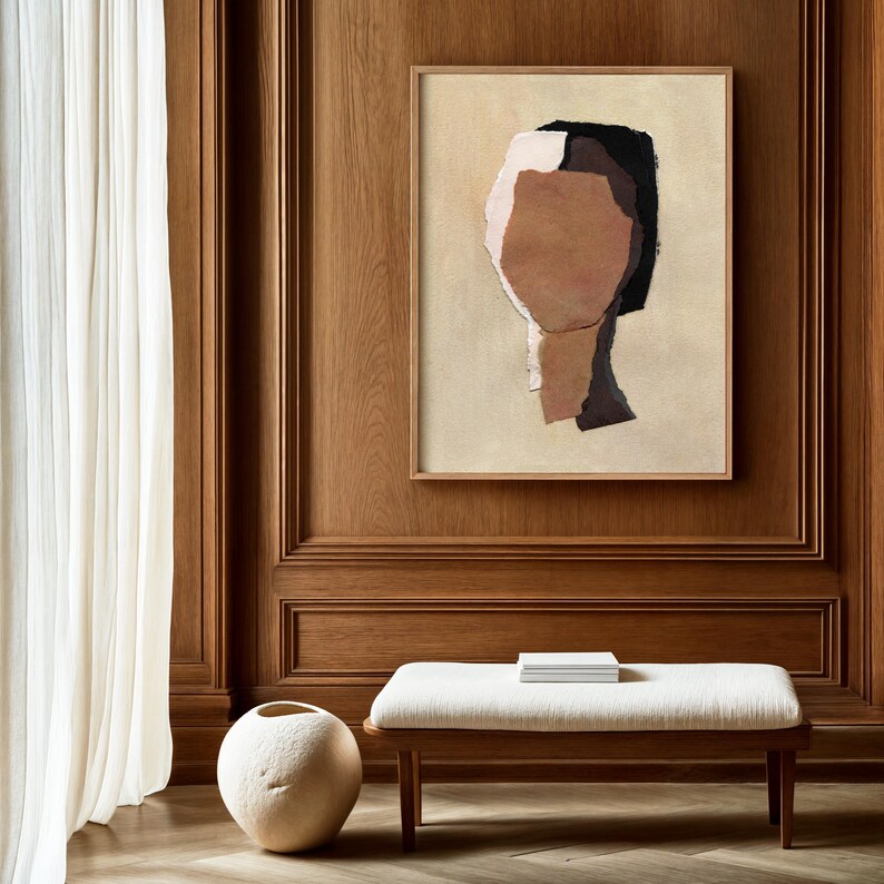 May include: Abstract art print featuring a collage of neutral tones, including beige, brown, and black, within a wooden frame. The artwork is mounted on a wood-paneled wall, complemented by a white bench and a decorative vase.