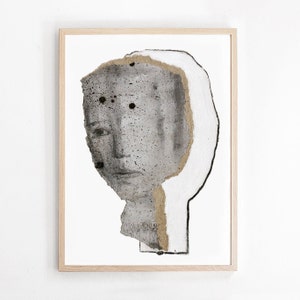 A golden framed high quality art print of a contemporary abstract zen portrait in shades of gray. A layer of ripped thick paper has golden ochre rough edges and graphite sketched facial features. A bigger head shape behind is outlined with charcoal.