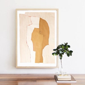 An interior wall art with a fine quality print of an abstract portrait. It is in a tender peach yellow pallet, with torn paper edges in cherry red, a pencil drawn eye for an accent. Layers in desert sand cut out a head from a pale peach background.