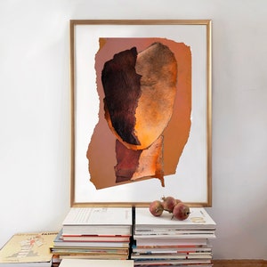 A studio decor with a high quality gold framed large wall art print of an abstract portrait in shades of vivid brown, varying from dark wood to blazing orange. A reddish drop spills out from the torn paper, random-shaped, faded persimmon background.