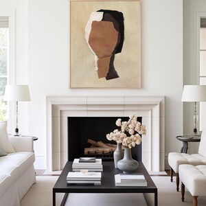 May include: Abstract art piece featuring a neutral color palette. The artwork, in a wooden frame, depicts a stylized human form with shades of brown, black, and white. The painting hangs above a fireplace, complementing the room's minimalist decor.