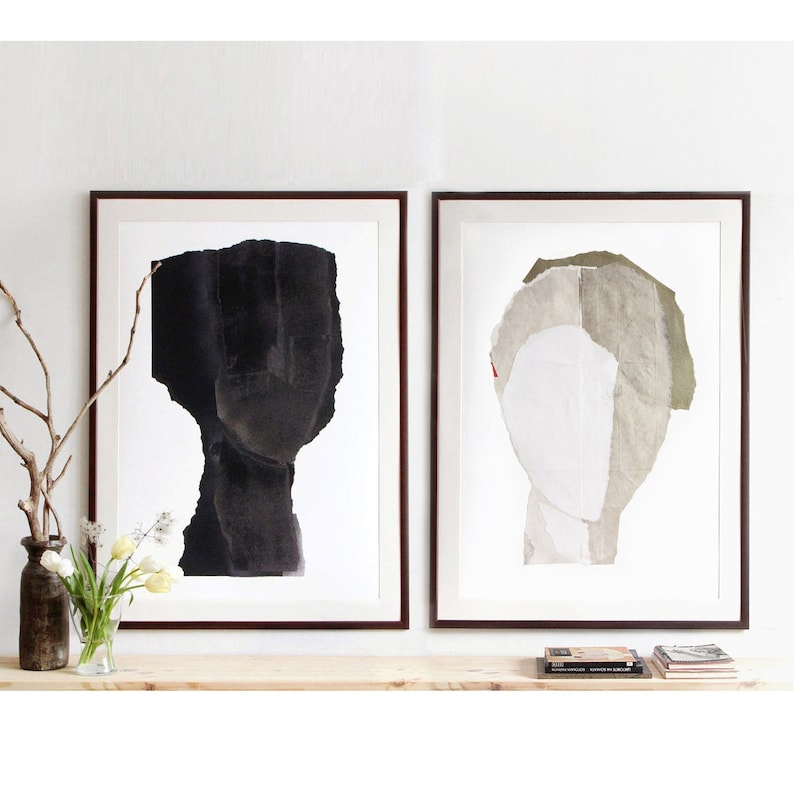 A neutral wall art with two black framed high quality art prints of abstract portraits in black scale, off white and greige. The layers of ripped paper has coarse contours. The set is balanced and neutral, best for wall decor.