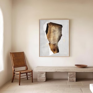 May include: A brown and white abstract art print in a light wood frame hangs on a white wall above a light brown wooden bench. The bench is made of stacked stone-like blocks.