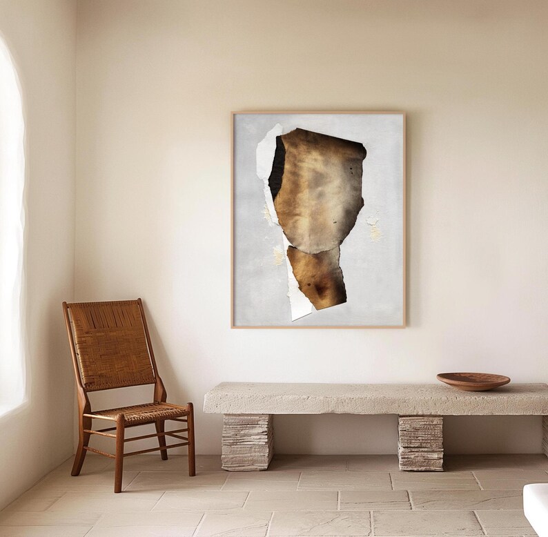 May include: A brown and white abstract art print in a light wood frame hangs on a white wall above a light brown wooden bench. The bench is made of stacked stone-like blocks.