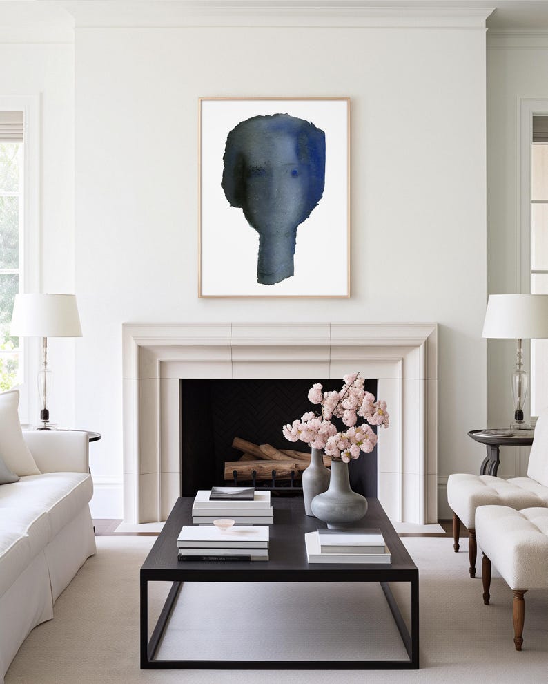 Puede incluir: Una habitaci&oacute;n blanca con una chimenea y una mesa de caf&eacute; negra. La chimenea tiene un hogar negro y una repisa blanca. Hay dos sillones blancos y un sof&aacute; blanco en la habitaci&oacute;n. Una pintura de acuarela enmarcada de una cara azul cuelga sobre la chimenea.