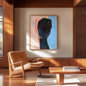 K&ouml;nnte beinhalten: Ein Wohnzimmer im Stil der Mid-Century Modern mit einem braunen Ledersessel, einem Holz-Couchtisch und einem gerahmten abstrakten Gem&auml;lde eines blauen und rosafarbenen Gesichts an der Wand.