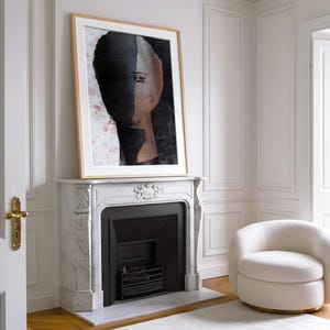 May include: A framed abstract painting of a face with a black and brown background. The painting is hanging above a white marble fireplace with a black fireplace insert.