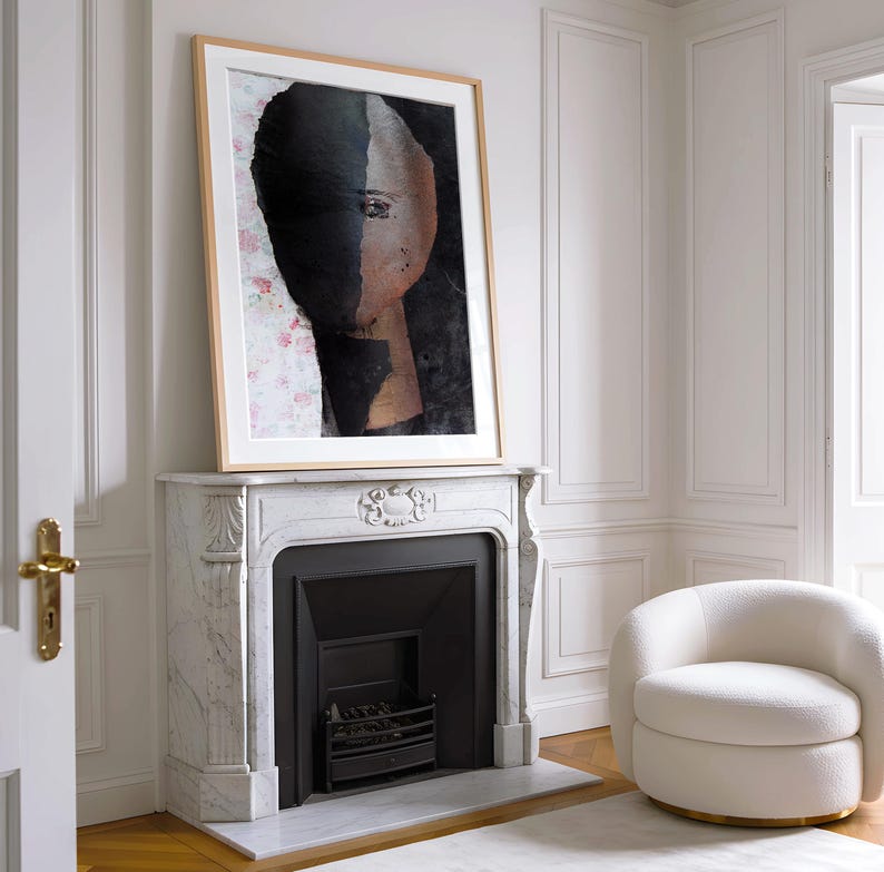 May include: A framed abstract painting of a face with a black and brown background. The painting is hanging above a white marble fireplace with a black fireplace insert.
