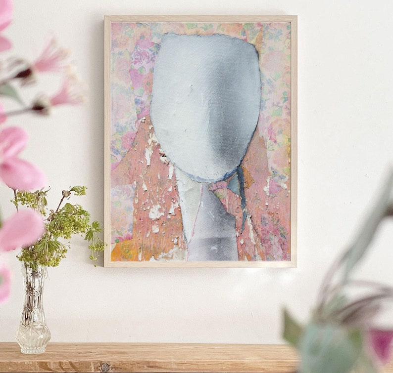 A balanced wall decor with a framed high quality archival art print of a feminine abstract portrait in pastel tones of pink, off white and dove grey on a floral background with violet and orange. It is made of torn paper pieces, rich in texture.