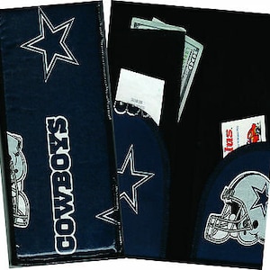 May include: A black and blue Cowboys wallet with a star and a football player on the front. The wallet has a zippered pocket on the back and a slot for cash and cards.