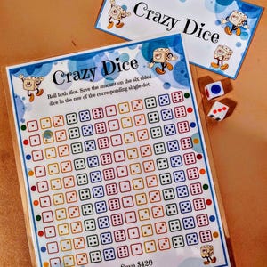 Puede incluir: Un juego de Crazy Dice con dos dados y dos tarjetas impresas. Las tarjetas muestran el texto "Crazy Dice" e instrucciones. El tablero del juego tiene una cuadrícula de cuadrados con patrones de dados y el texto "Save 420$ Save With Judy".