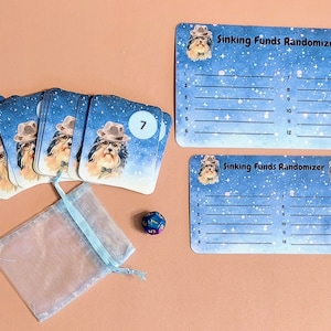 May include: A set of 12 cards with a dog wearing glasses and a hat on each card. The cards are blue with white stars and the text "Sinking Funds Randomizer". There is a blue dice with white numbers and a blue bag.