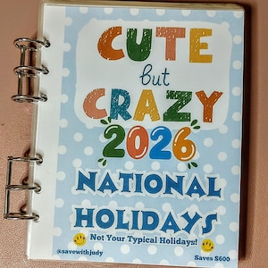 May include: A spiral-bound planner with a light blue cover. The cover displays the text "CUTE but CRAZY 2026 NATIONAL HOLIDAYS" in colourful lettering. The design includes polka dots and the phrase "Not Your Typical Holidays!"
