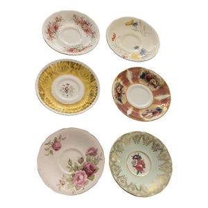 May include: A collection of six vintage teacup saucers. The saucers display floral and gold patterns, with colours including pink, gold, and green. The designs feature roses, butterflies, and other botanical elements. Ideal for tea parties or as decorative pieces.