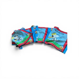 May include: Blue and red Peanuts All-Stars themed fabric. The fabric features Snoopy and other Peanuts characters playing sports. The fabric has a red border and the words "Peanuts All-Stars" are visible.