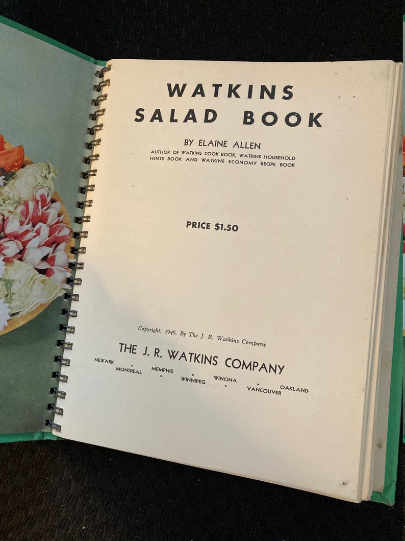 May include: A vintage Watkins Salad Book with a green cover and a spiral binding. The book is open to the title page, which features the title "Watkins Salad Book" in large, bold letters. The author, Elaine Allen, is listed below the title, along with the price, $1.50. The copyright information is at the bottom of the page, indicating the book was published in 1946 by The J. R. Watkins Company.