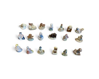May include: A collection of twenty miniature ceramic figurines arranged in three rows. The small, hand-painted figures feature various shapes, including people, animals, and objects, rendered in muted tones of blue, brown, tan, and white.